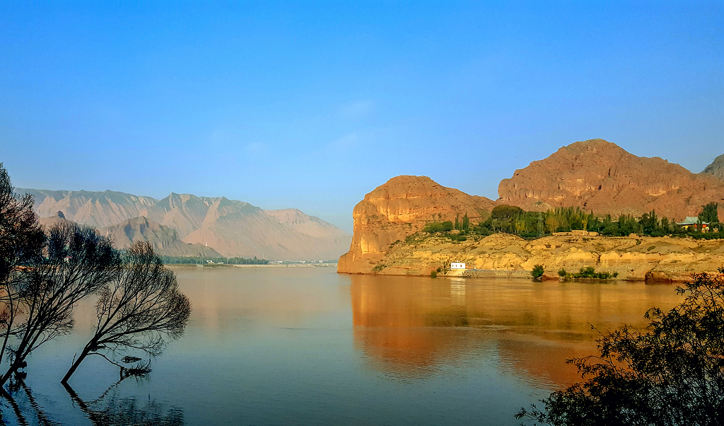 夏日的清晨阳光照在黄河岸边的山坡和小山村并倒影在水面上