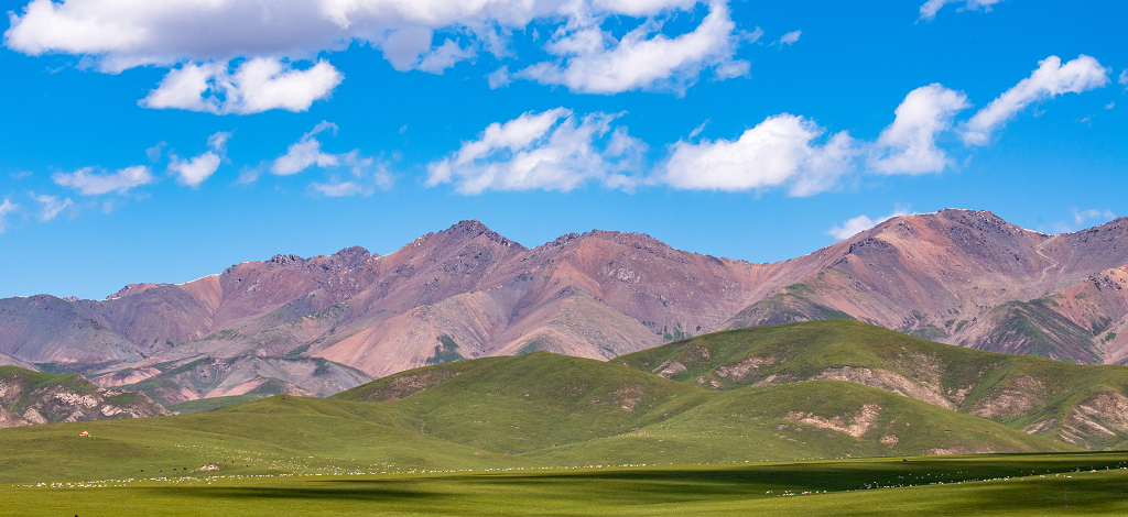 夏日的蓝天白云远方暗红色的石山和草原上成群结队的牛羊