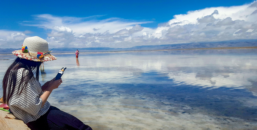 夏日的午后一少女做在河岸边蓝天白云倒影在茶卡盐湖湖面上