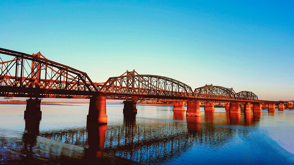 秋日的日落时分晚霞染红了鸭绿江大桥倒影在河水中