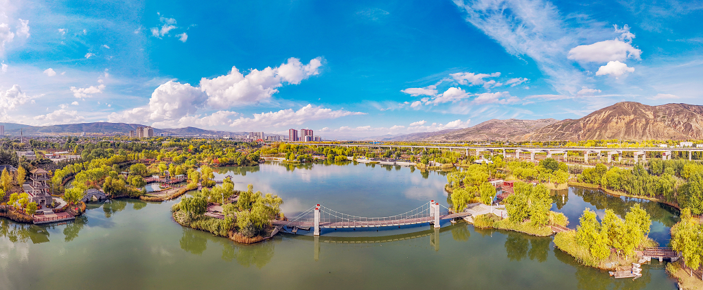 金秋时节蓝天白云航拍湿地公园的树木吊桥和流水及景观