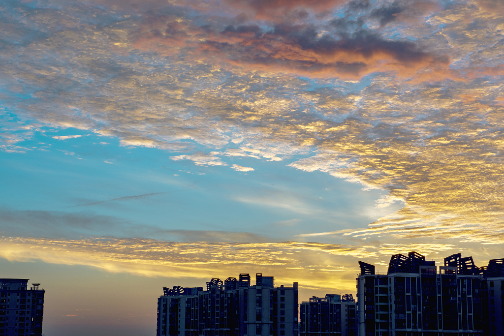 日出时分天空椭圆形的彩色云朵下城市建筑物剪影
