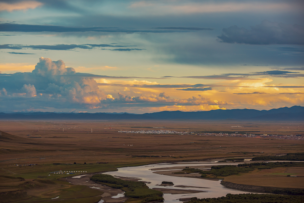 傍晚的日落时分阴影中的草原及弯曲的河流和天空彩色的云彩