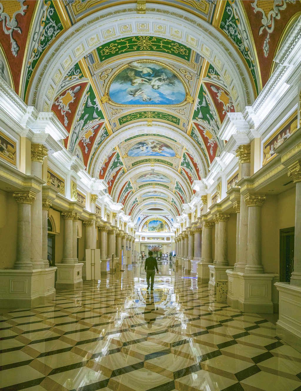 酒店长廊拱形顶部的壁画下一游客走过并倒影在地板上