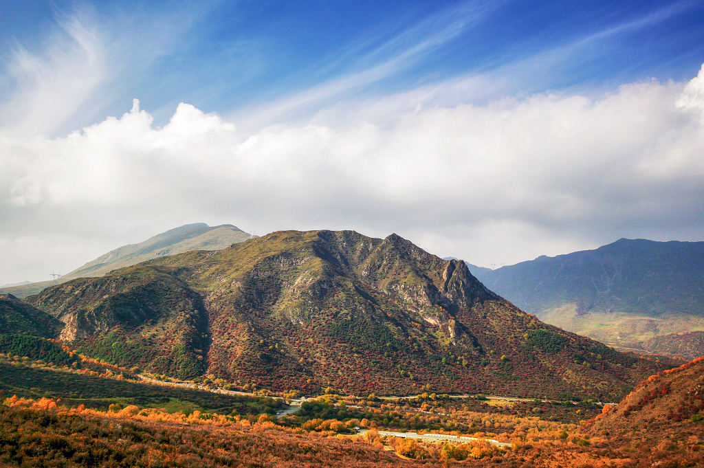 晴天的清晨蓝天白云阳光照亮了山峰和山谷中金黄色的灌木丛