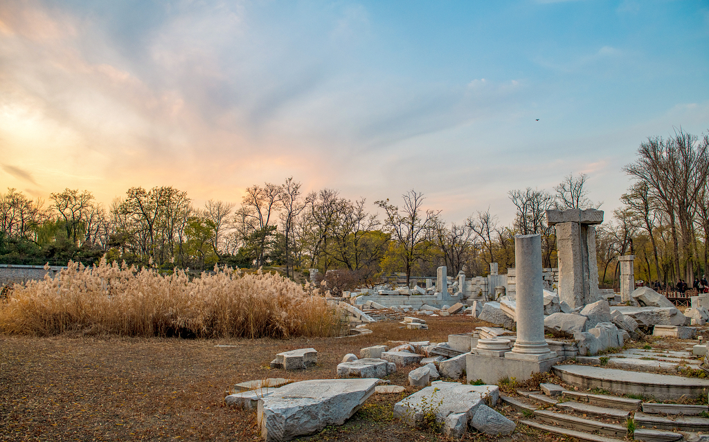 晚霞时分天空五颜六色地面上被破坏的圆明园残骸和树木