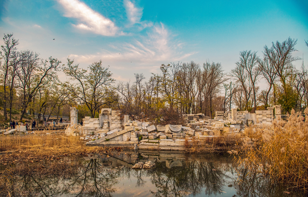 晚霞时分天空五颜六色地面上被破坏的圆明园残骸和树木