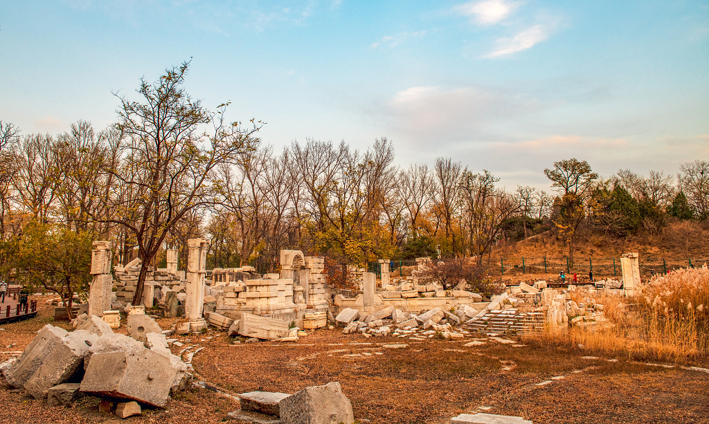 晚霞时分天空五颜六色地面上被破坏的圆明园残骸和树木