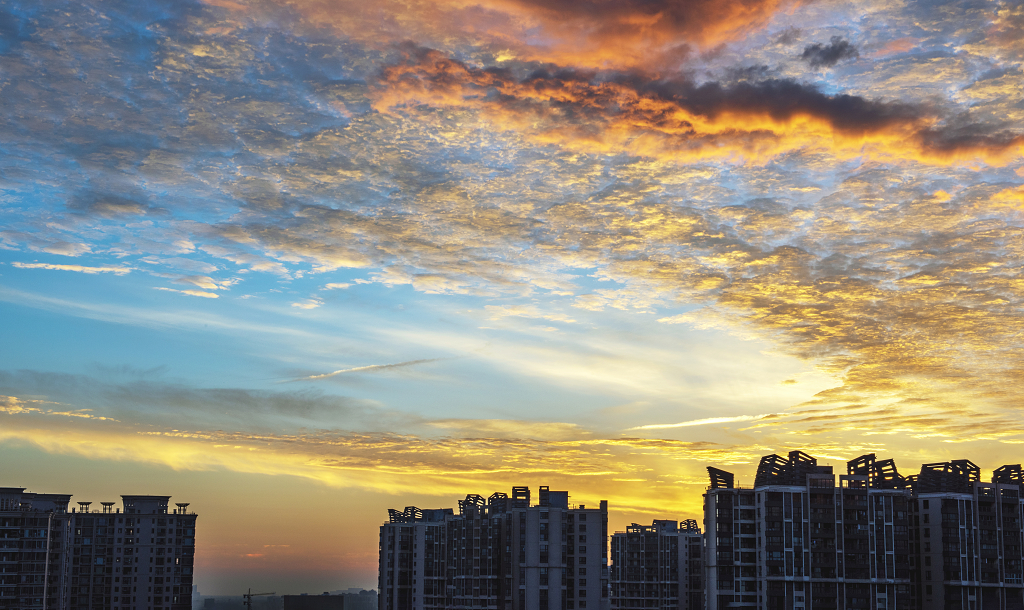 夏日的日出时分城市上空的金黄色的彩云和建筑物剪影