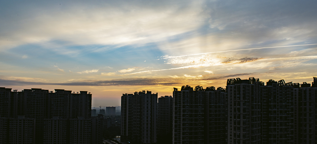 夏日的日出时分城市上空的放射状的彩云和建筑物剪影
