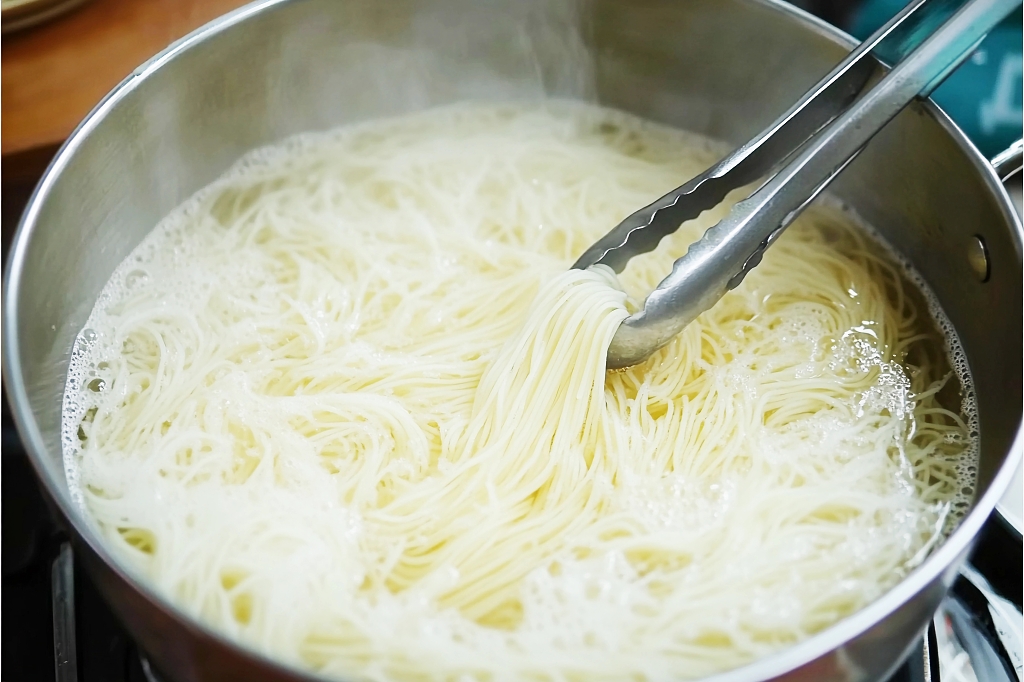 不锈钢锅中用夹子烹煮着的白色细面条AI