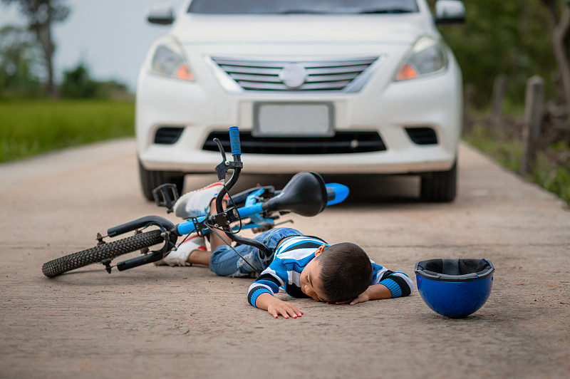 一个男孩在路上因自行车与汽车相撞而受伤。一个亚洲男孩被车撞了。道路事故的概念和减少事故从使用汽车在道路上。有选择性的重点。