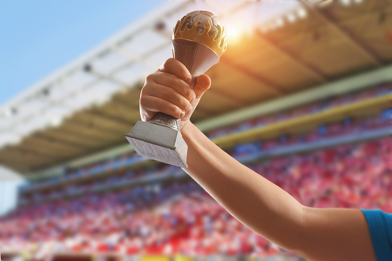 孩子举起手，捧着金色的足球杯对着天空。奖励和胜利的概念