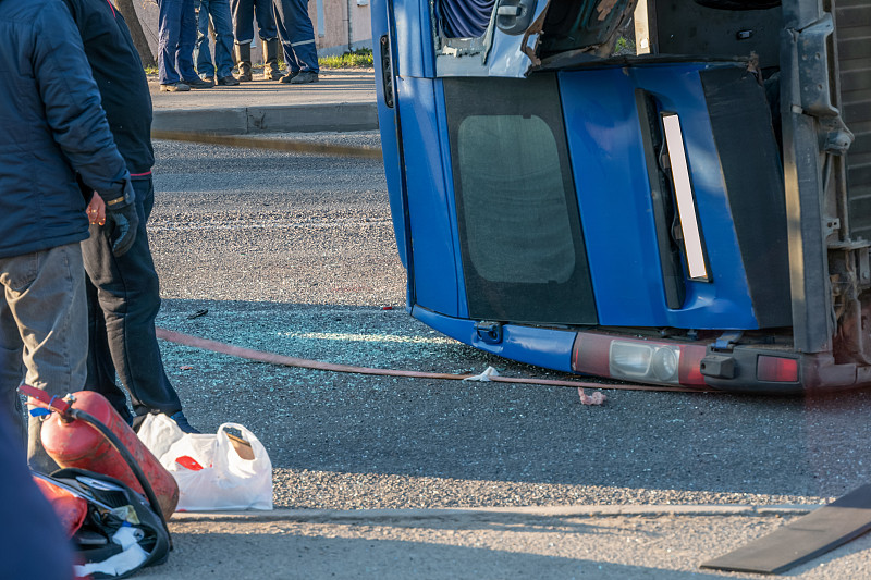 一辆倒车的蓝色小货车在路上，人们的双腿离得很近