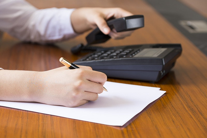 女人用笔在纸上记录和打电话