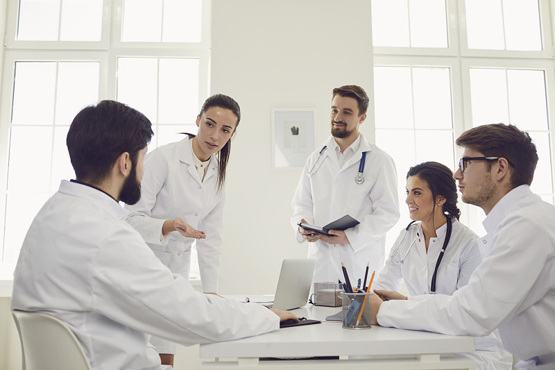 一群执业医生在会议上讨论一个站在诊所办公室的病人的诊断。