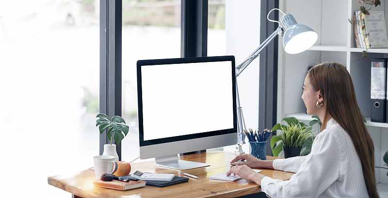 女商人在台式电脑上工作，坐在现代的办公室里。