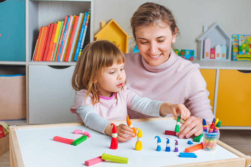 快乐的母亲和四岁的小女孩用孩子的玩具粘土塑造了五颜六色的地精