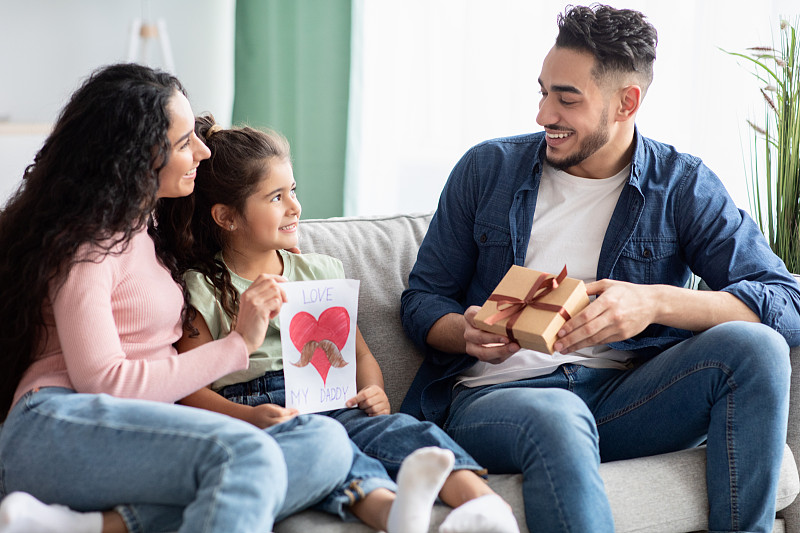 父亲节。快乐的阿拉伯母亲和女儿给快乐的人礼物
