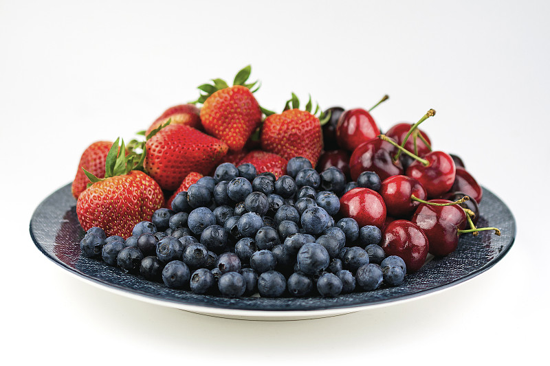 一个有蓝莓、草莓和樱桃图案的蓝色盘子，在白色的背景上。