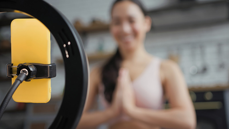 健康的亚洲瑜伽女人坐在莲花的位置和做在线瑜伽课。专注于手机。合十礼