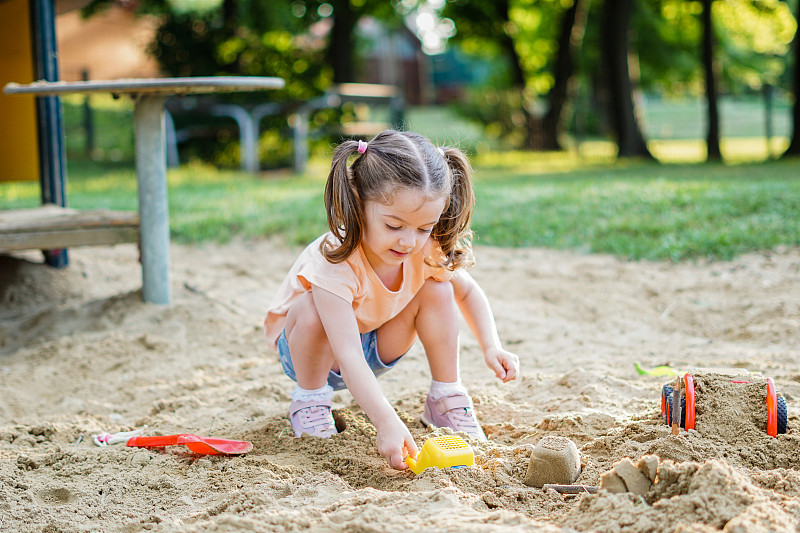 美丽的宝宝在阳光温暖的夏天玩得很开心-可爱的蹒跚学步的女孩在户外操场上玩沙子