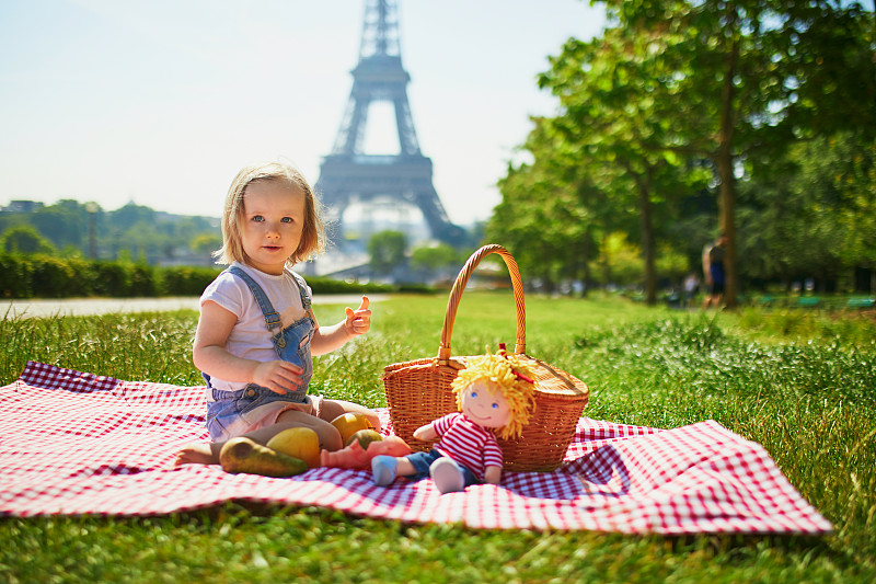 快乐的蹒跚学步的小女孩在巴黎埃菲尔铁塔附近野餐