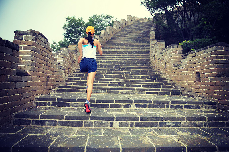年轻的女子越野跑运动员在山顶的长城上奔跑