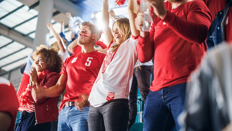 体育场大事件:一群球迷为红色足球队的胜利欢呼。人们庆祝进球，冠军。可爱的白种人夫妇涂了脸欢呼，欢呼。