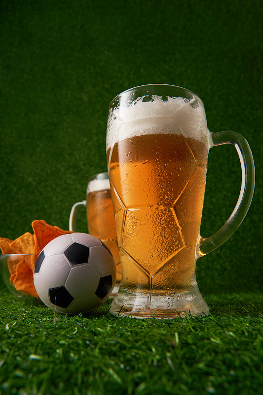 两杯啤酒，绿草地上放着足球。