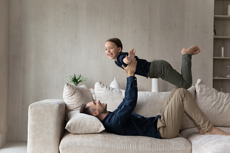 快乐的年轻拉丁父亲举在空中笑着可爱的小女儿。