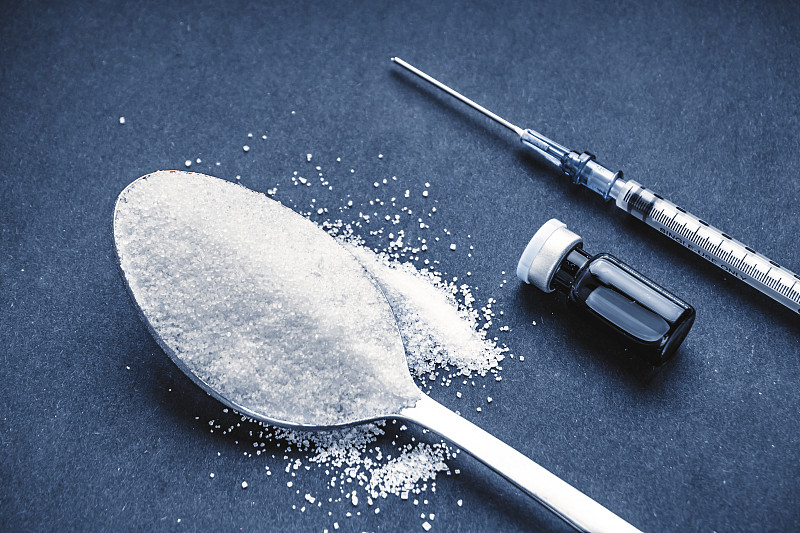 极简平铺合成糖，勺子，注射器和小瓶在黑暗的背景