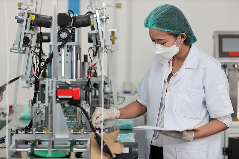 穿着个人防护装备或个人防护用品的女工检查工厂口罩和医用口罩生产线的质量，制造业和工厂理念。