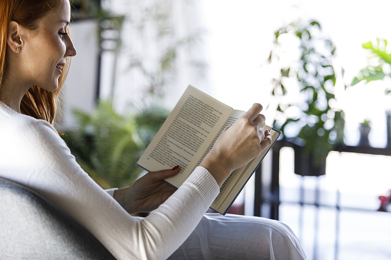 复制空间的照片，微笑的红头发在读一本有趣的书，同时放松
