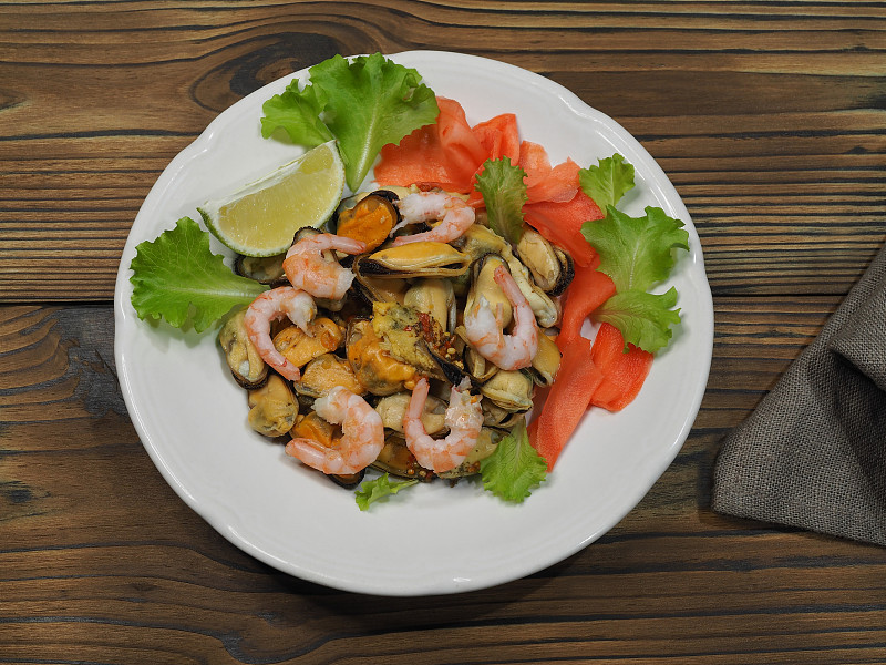 简单的沙拉，带皮的贻贝，腌生姜和青柠，放在木桌上的白色盘子里，平面布局。食谱为清淡小吃配以美味的海鲜，适宜饮食营养，俯视图