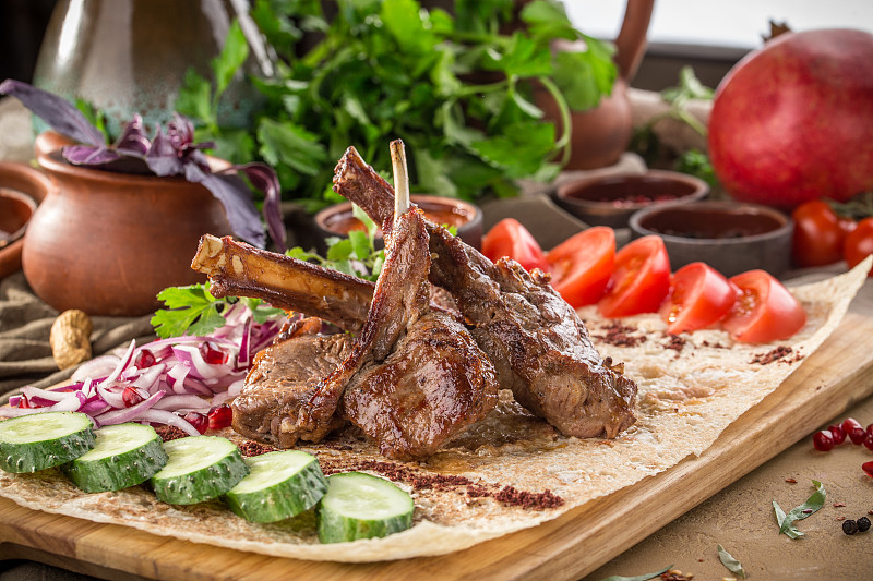 烤羊排骨配红洋葱、黄瓜、番茄和番茄酱，放在木桌上