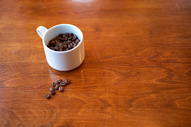 木质桌子上放着装满咖啡豆的白咖啡杯