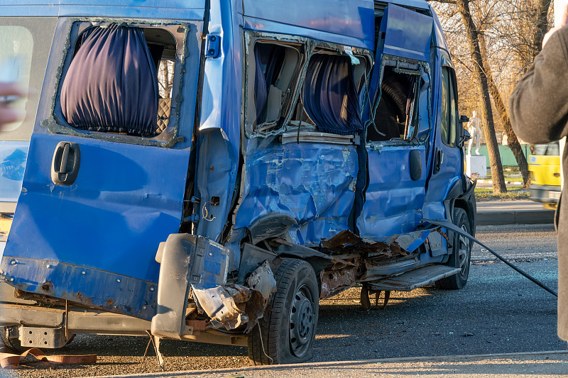 一辆被撞皱的蓝色小巴在路上。在一个阳光明媚的日子，在城市的道路上发生了事故。一辆卡车与一辆小型公共汽车相撞，又与一辆小汽车相撞。