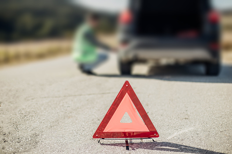 一名男子在街上的警示牌后面检查一辆破车的轮胎