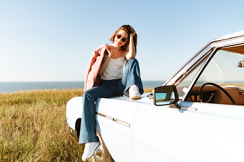 时尚漂亮的女人放松，而坐在汽车户外