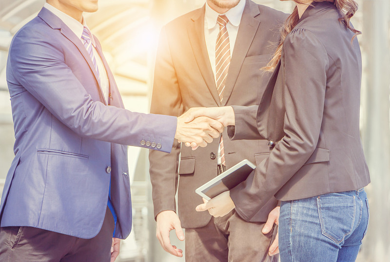 成功和幸福的团队概念，近距离的商人握手与女商人站在他们旁边模糊的城市背景