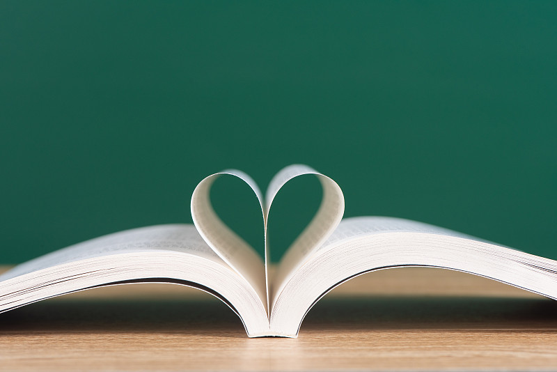 打开书在绿色黑板背景下的木制书桌上