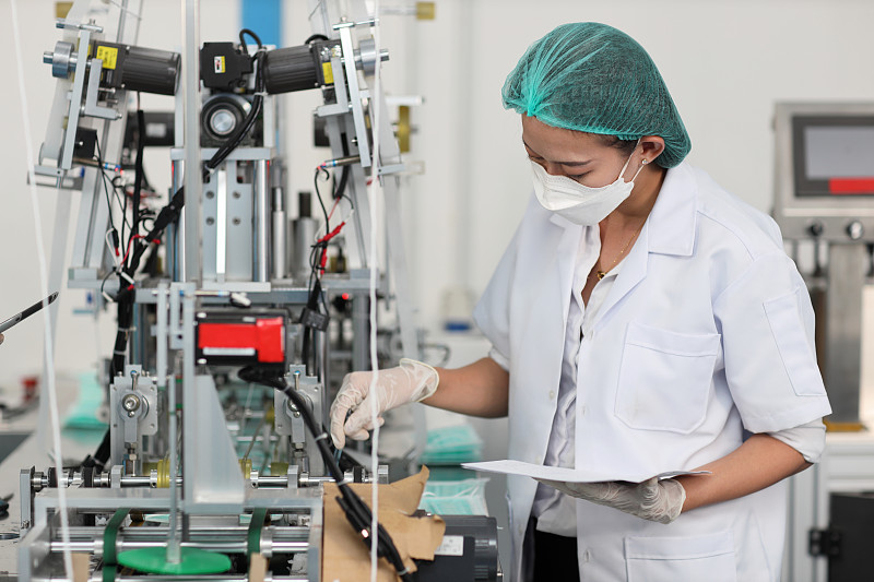 穿着个人防护装备或个人防护用品的女工检查工厂口罩和医用口罩生产线的质量，制造业和工厂理念。