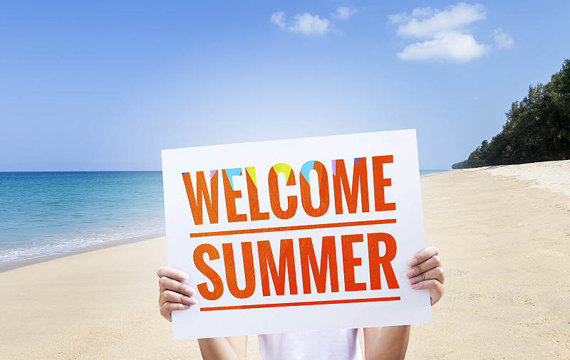 女孩拿着欢迎夏天的标志在海滩背景