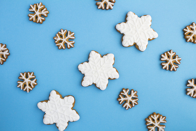 蓝色的背景上是扁平的圣诞雪花形状的姜饼