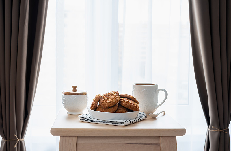 早餐的咖啡和饼干放在卧室的一张挂着窗帘的木桌上