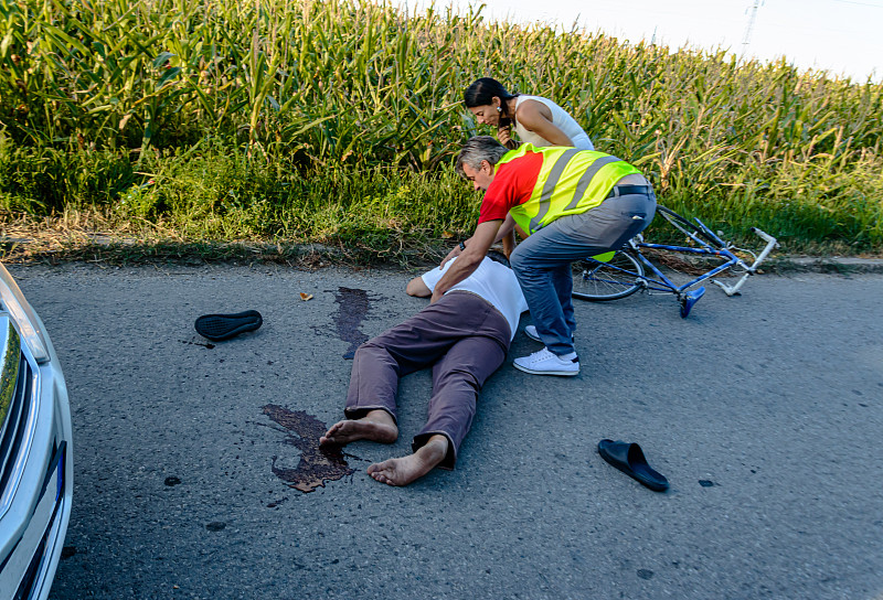 一个女人和一个男人在路上帮助一个发生事故的骑自行车的人。