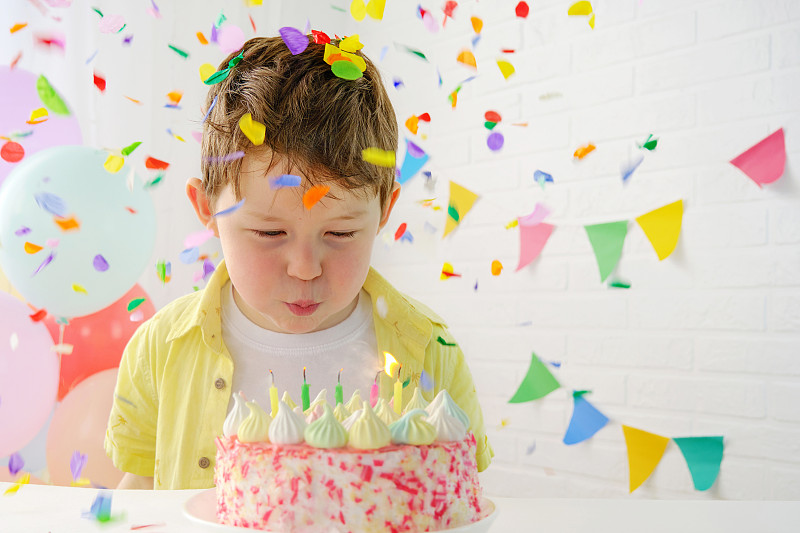 孩子吹熄了生日蛋糕上的蜡烛。5岁的男孩在节日的环境中。生日，五彩纸屑落在男孩身上。水平的照片。