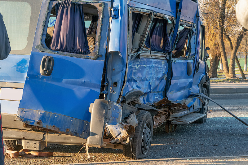 一辆被撞皱的蓝色小巴在路上。在一个阳光明媚的日子，在城市的道路上发生了事故。一辆卡车与一辆小型公共汽车相撞，又与一辆小汽车相撞。