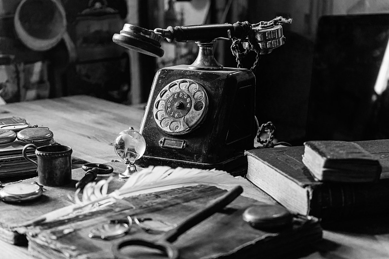 古董书桌与配件:旧电话，书，地球仪，笔记，钢笔，旧眼镜。和几个小时。这幅画传达了一种古老的气氛——过去的岁月